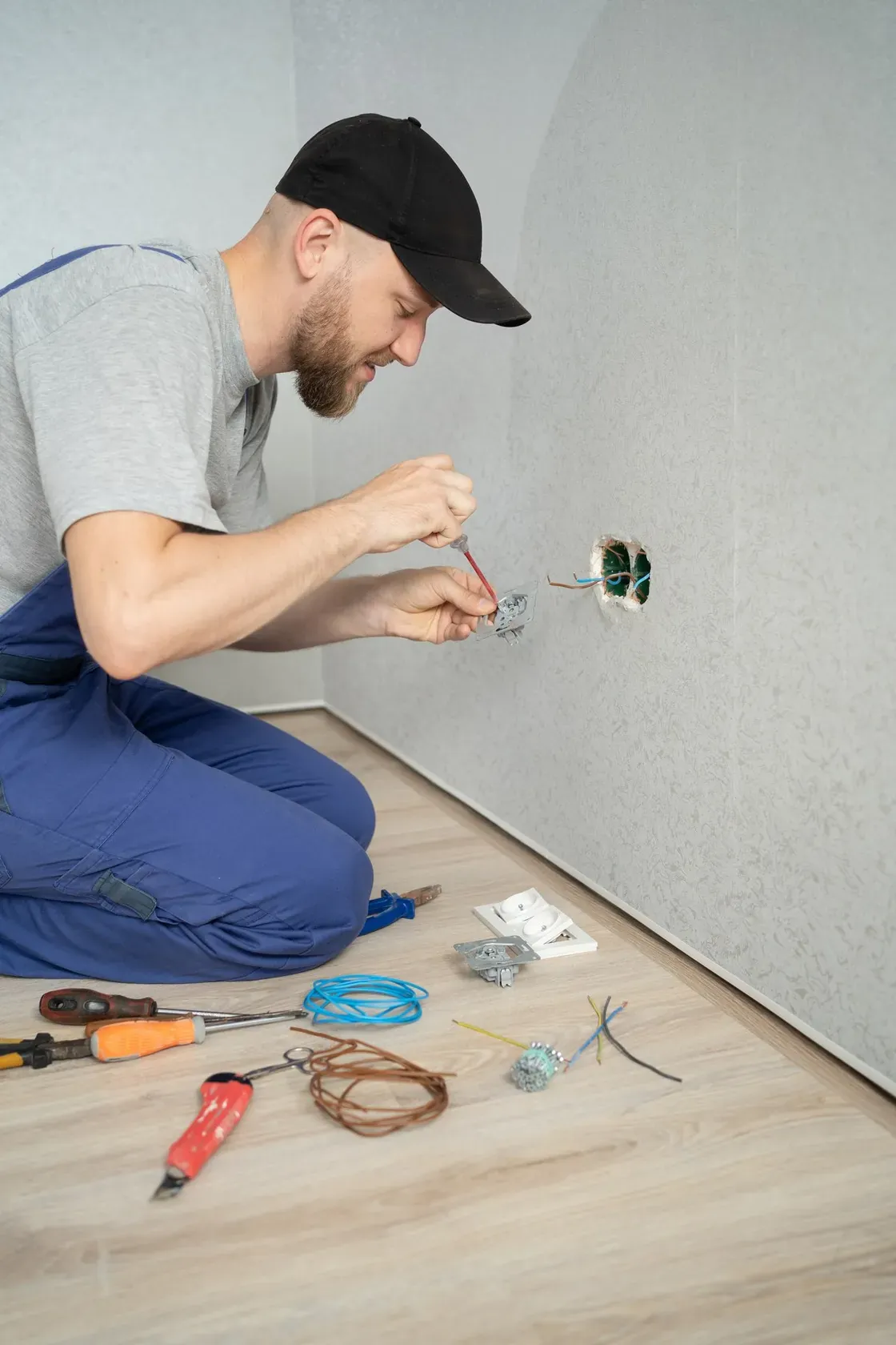 An electrician wiring an outlet box on a wall during a service call
