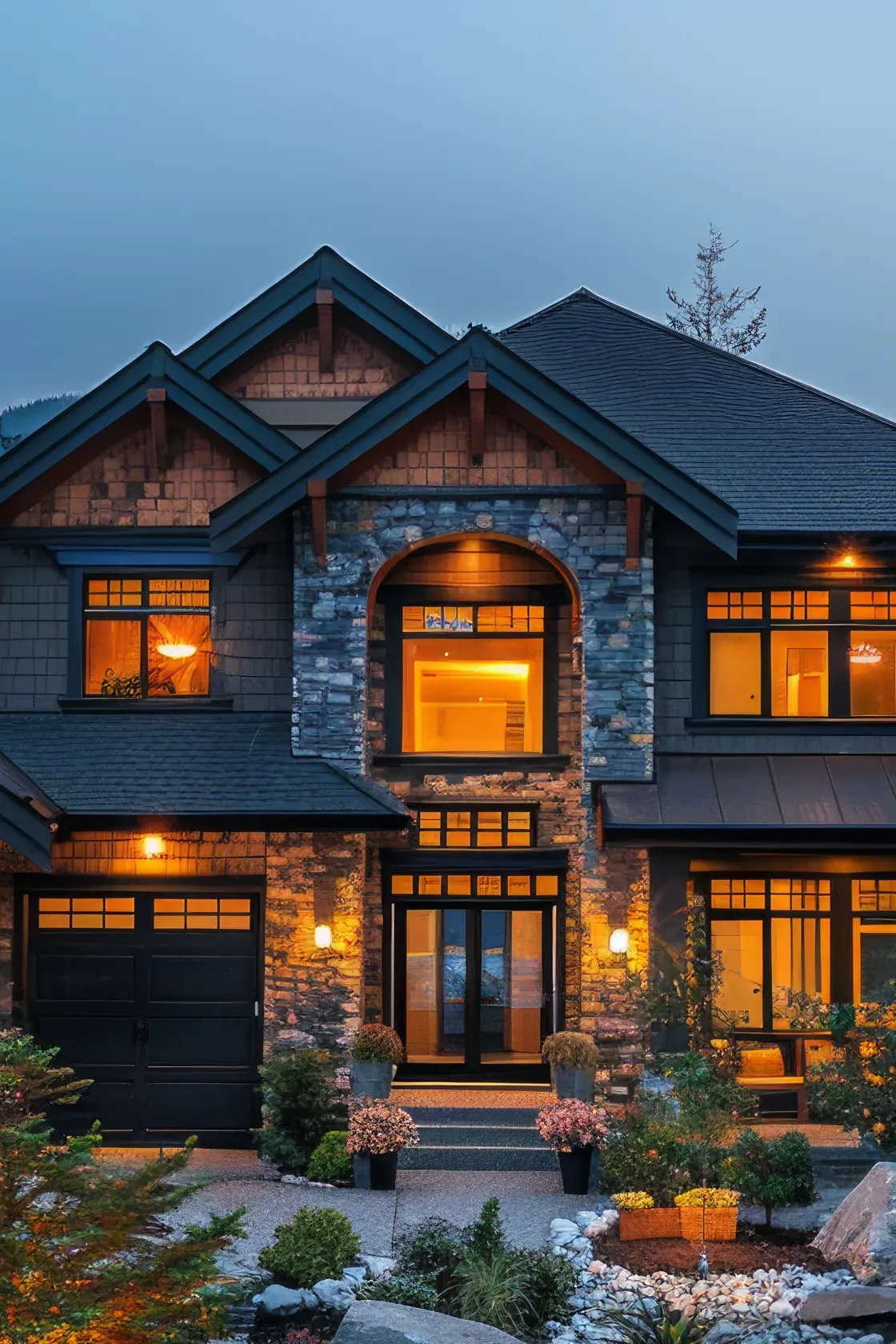 A finished two-story craftsman home with stone and cedar shake siding, its windows lit warm at dusk above a landscaped front walk