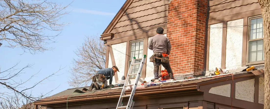 A roofer working on the back of a two-storey brick house